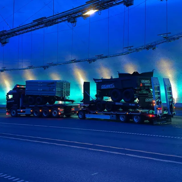 To Haugan-lastebiler med Gigant landbruksvogner på spesialhengere, parkert i fargerikt lyssatt tunnel.