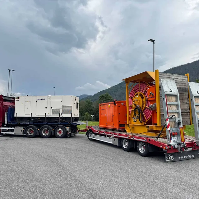 Lastebil med spesialhenger frakter Skanska-utstyr og kabeltrommel i industriområde.