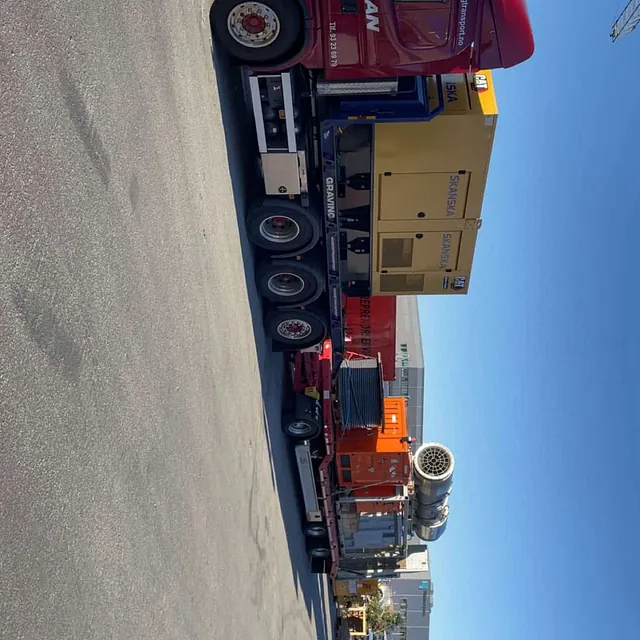 Rød Haugan-lastebil frakter Skanska-generator, orange utstyr og kabeltrommel på industriområde.